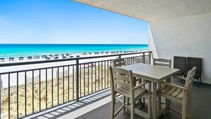 A balcony with a view of the beach, a table, and chairs.