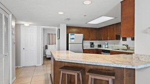A kitchen with wooden cabinets, a granite countertop, and a built-in bar area with stools.