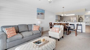 A modern living room with a grey sofa, white armchair, and a dining area with wooden chairs. - Islander Beach Resort 6012 (Fort Walton Beach)