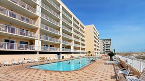 A hotel with a swimming pool, multiple balconies, and a beach view.