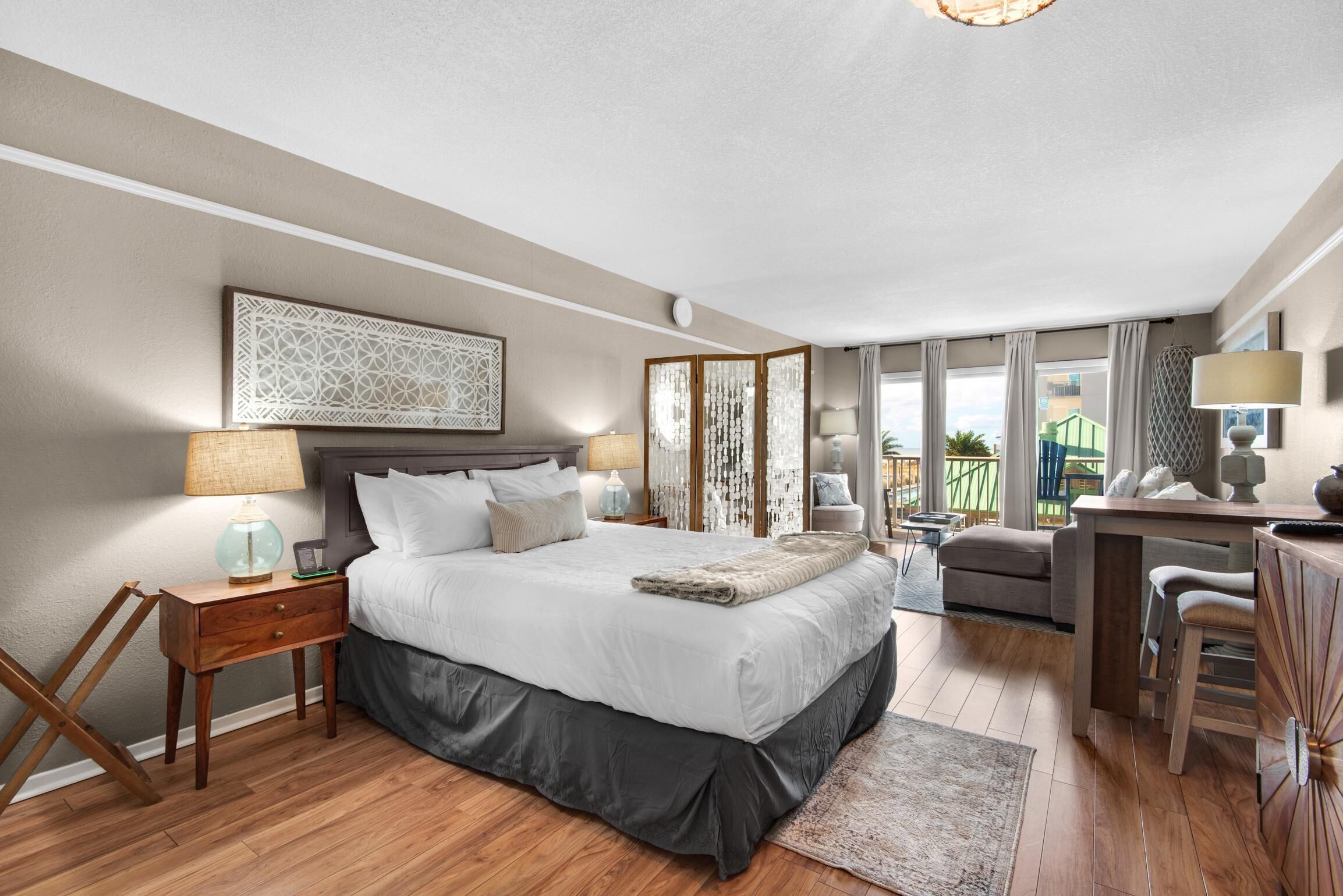 A bedroom with a large bed, bedside tables, a desk, and a view of the outdoors.