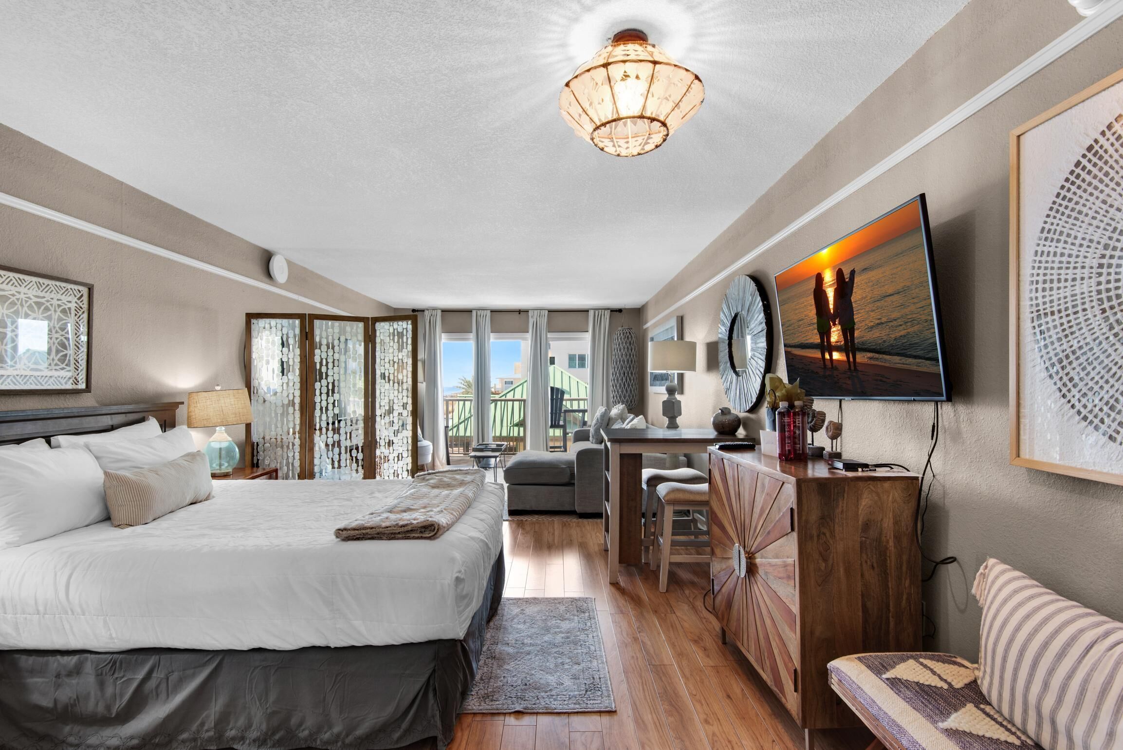A spacious bedroom with a large bed, a desk, a TV, and a view of the sea.