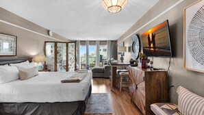 A spacious bedroom with a large bed, a desk, a TV, and a view of the sea.