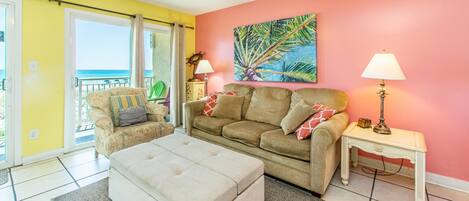 A living room with a sofa, ottoman, and a painting of a palm tree.