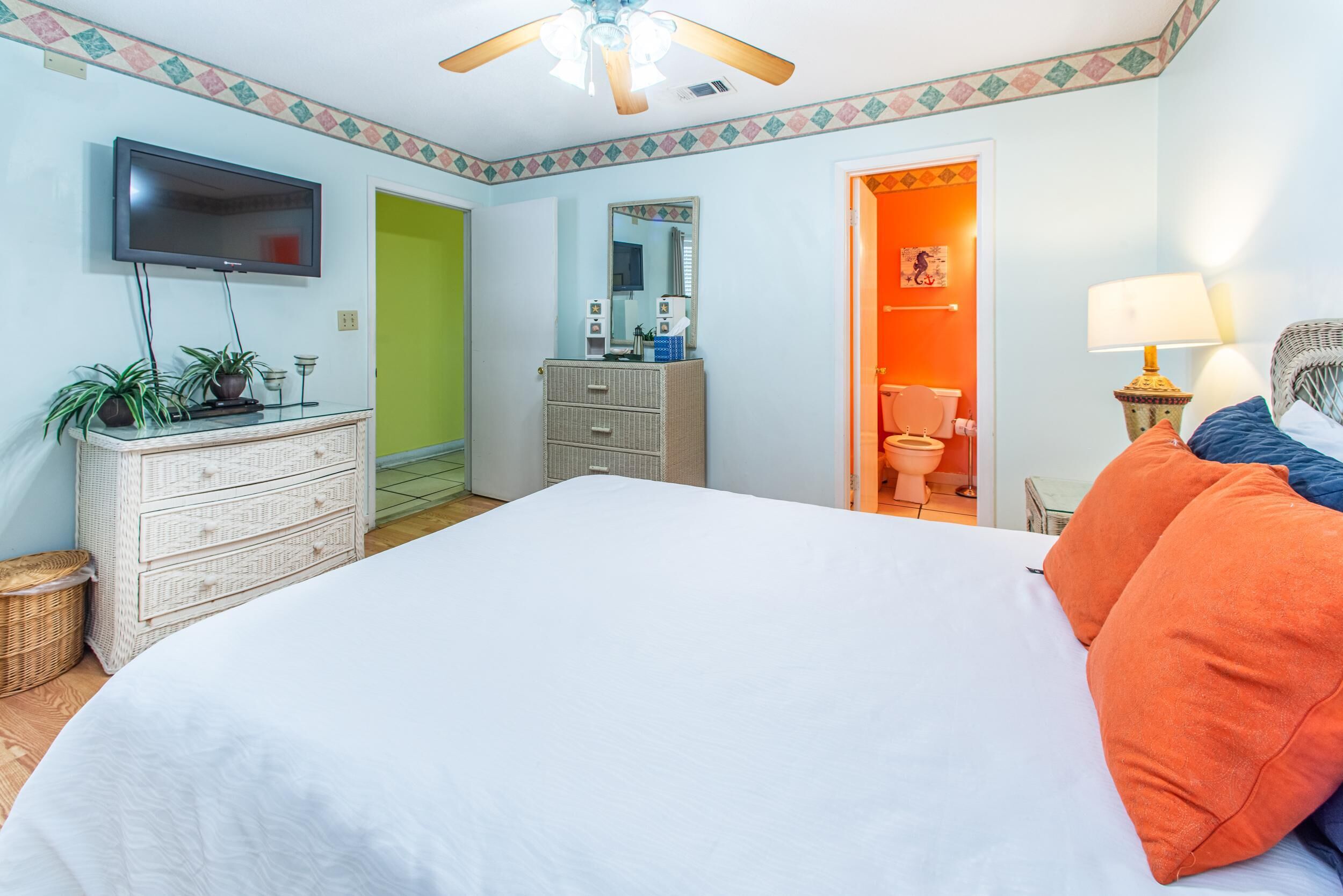 Un dormitorio con cama, cómoda, televisor y un baño visible a través de una puerta abierta.