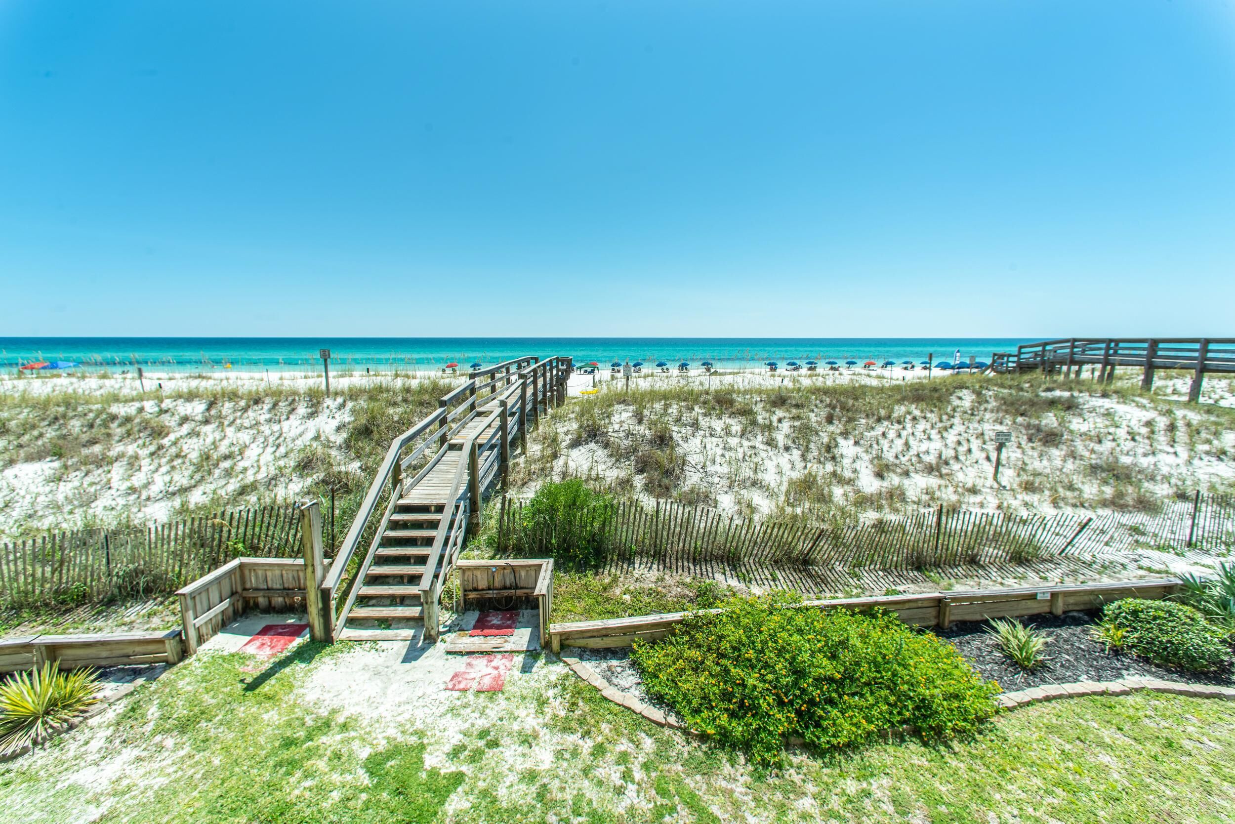 A beach with a wooden staircase leading down to the sand, a wooden fence, and a clear view of the ocean.