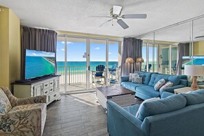A spacious living room with a large TV, comfortable seating, and a balcony with a view of the ocean. - Island Princess 506 (Fort Walton Beach)