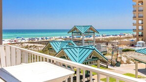 Vista sulla spiaggia con un edificio dotato di numerose stanze dai tetti verdi, una spiaggia sabbiosa e un cielo blu limpido.
