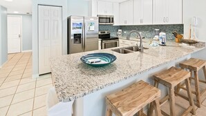 Una cucina moderna con mobili bianchi, elettrodomestici in acciaio inossidabile, un piano di lavoro in granito e sgabelli di legno.