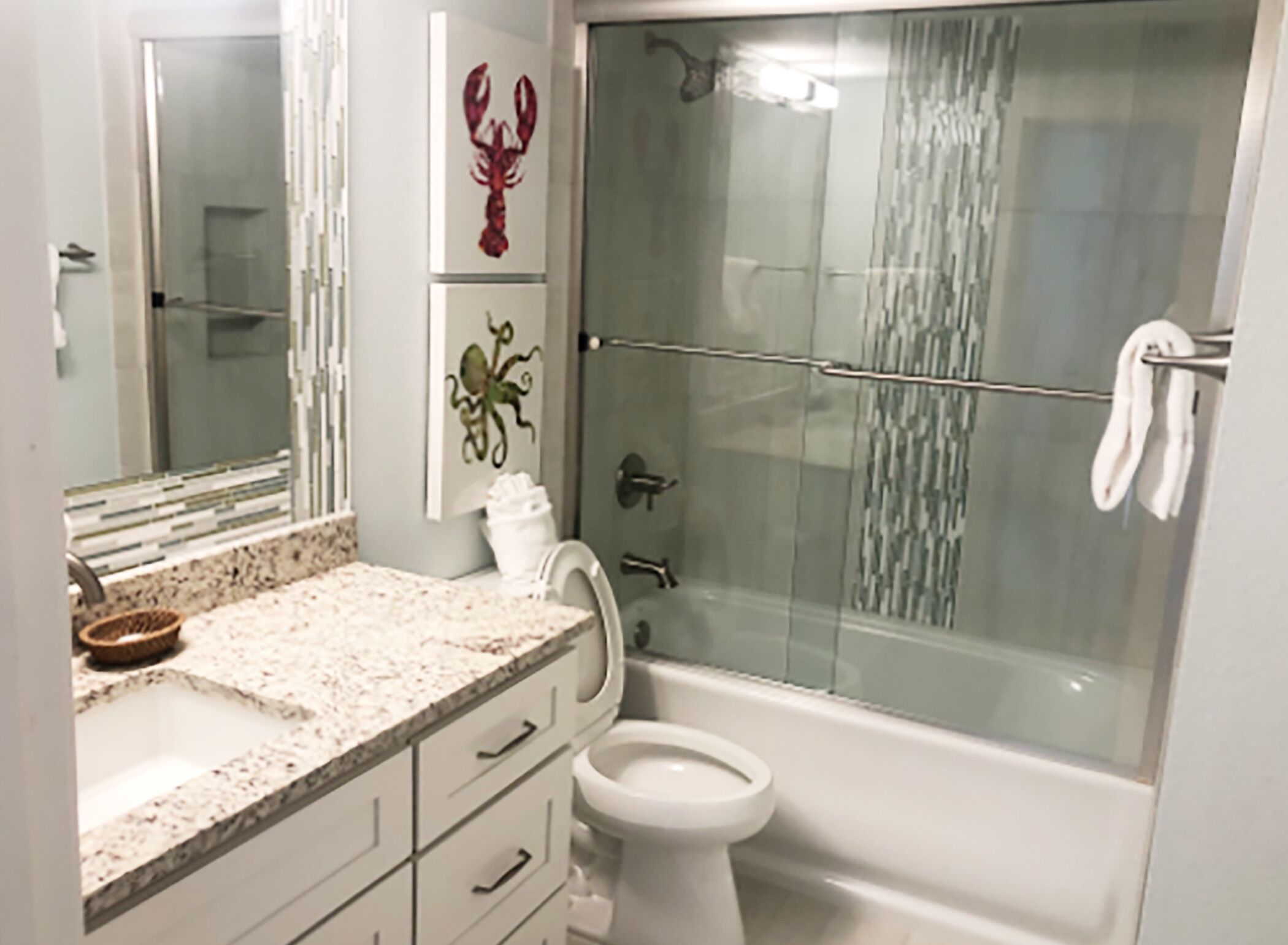 A bathroom with a glass shower enclosure, a toilet, and a sink with a marble countertop.