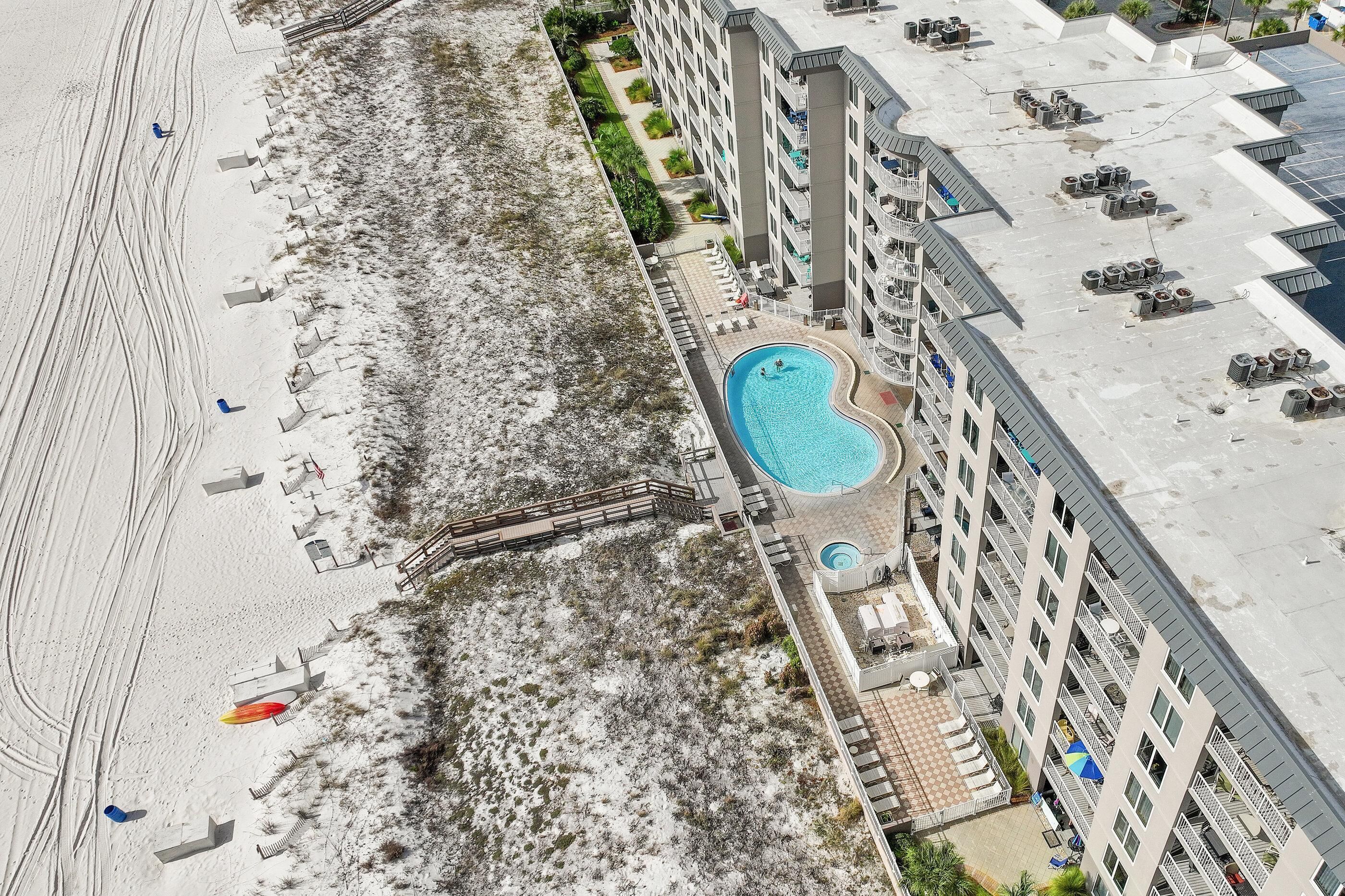 Luchtbeeld van een hotel met een zwembad, toegang tot het strand en een parkeerplaats.
