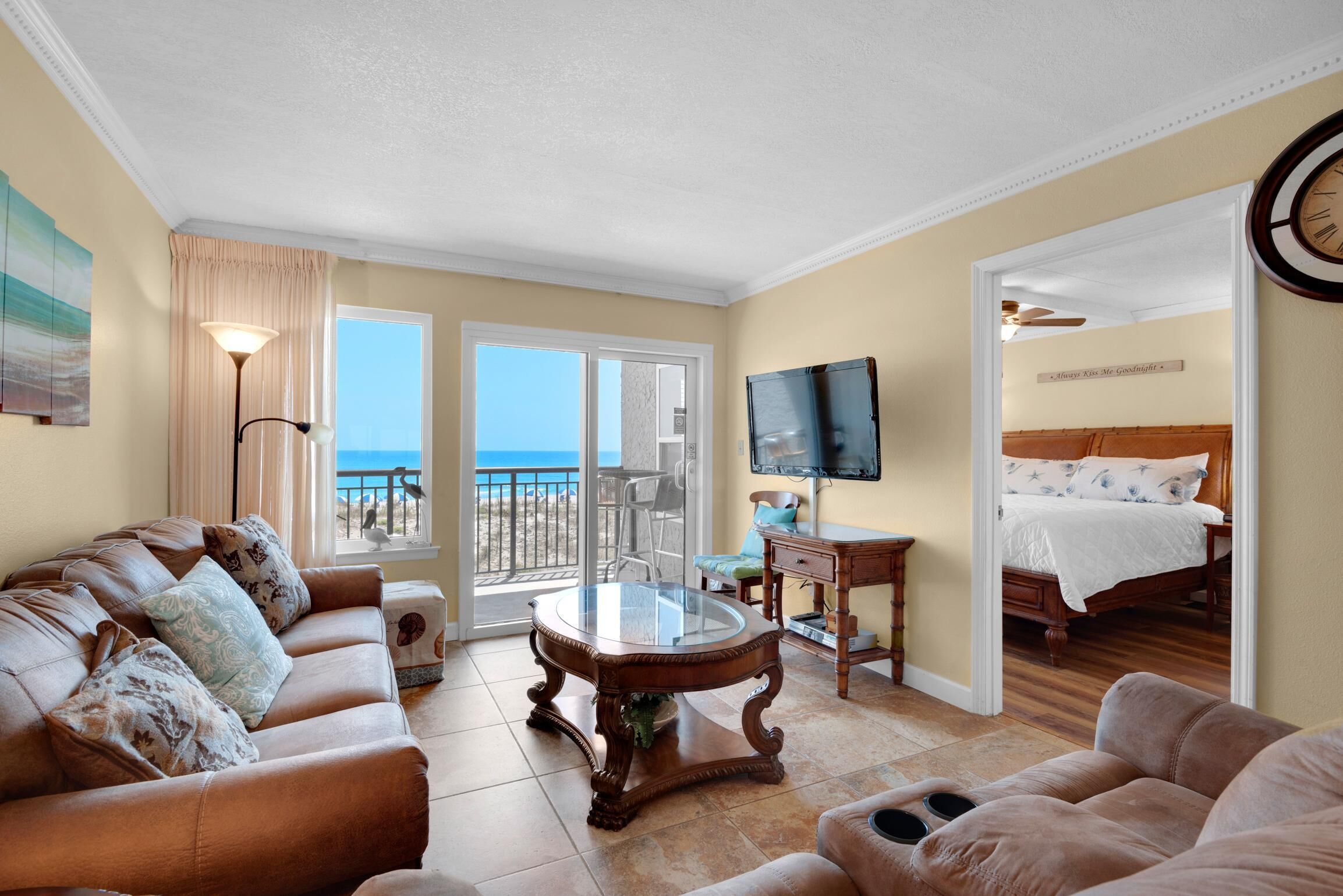 A spacious living room with a leather sofa, a glass coffee table, and a view of the ocean through large sliding doors.