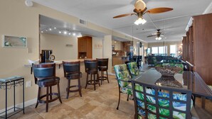 A spacious kitchen with a dining area, featuring a bar with stools, a large island, and ceiling fans. - Island Echos #2E (Fort Walton Beach)
