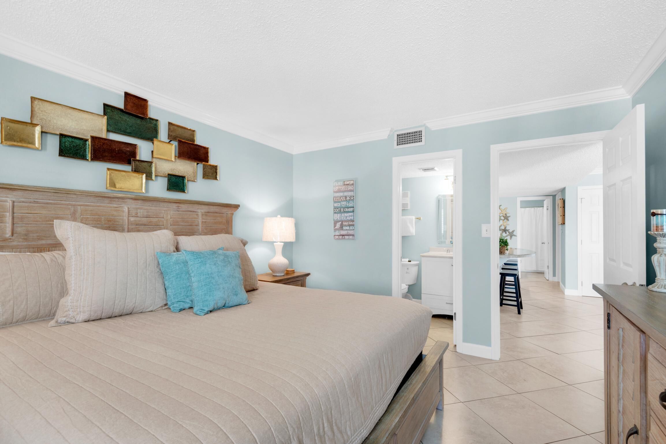 A bedroom with a large bed, a nightstand, a wall-mounted light, and a decorative wall piece.