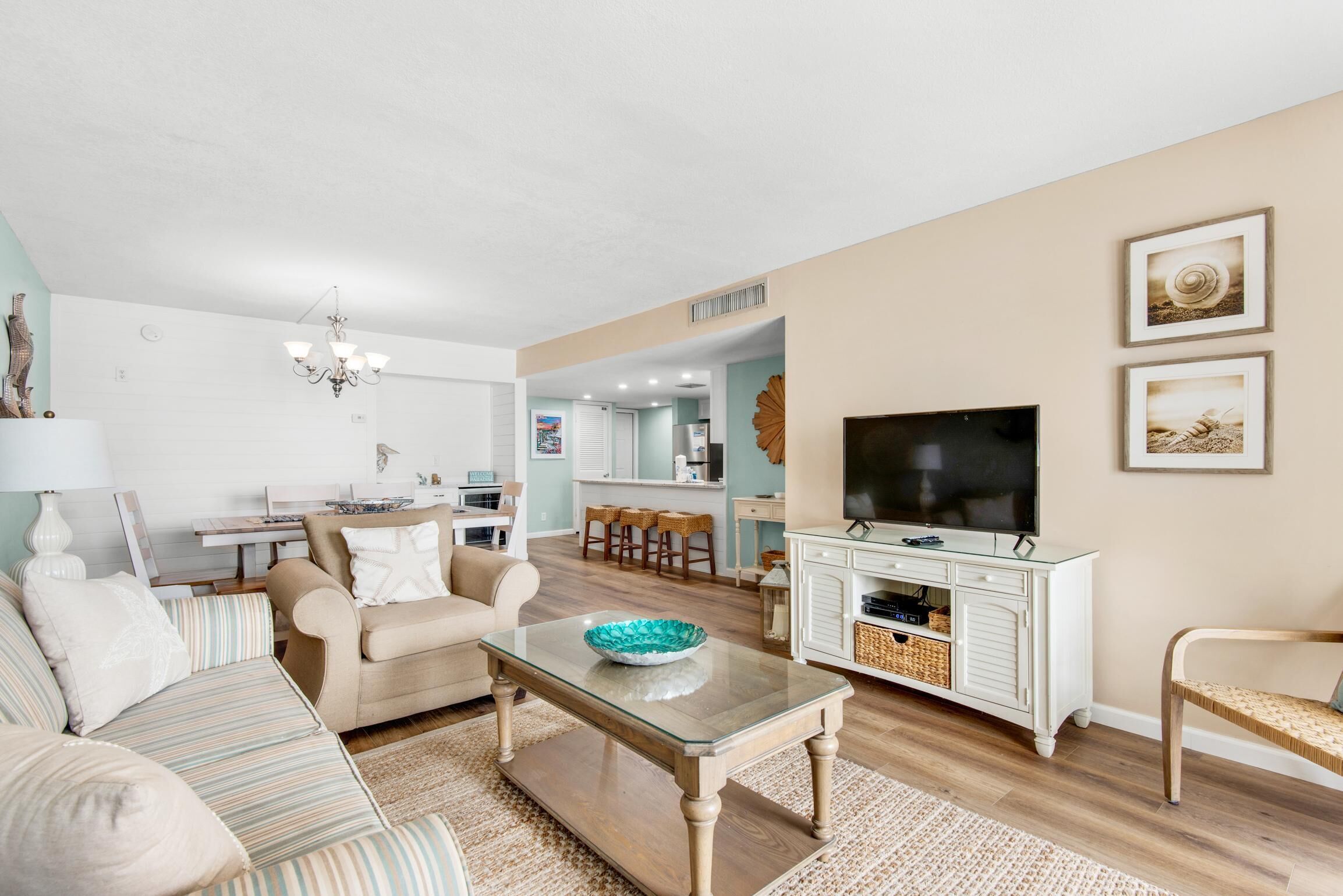 A modern living room with a sofa, coffee table, and TV. There is a kitchen area in the background with bar stools.