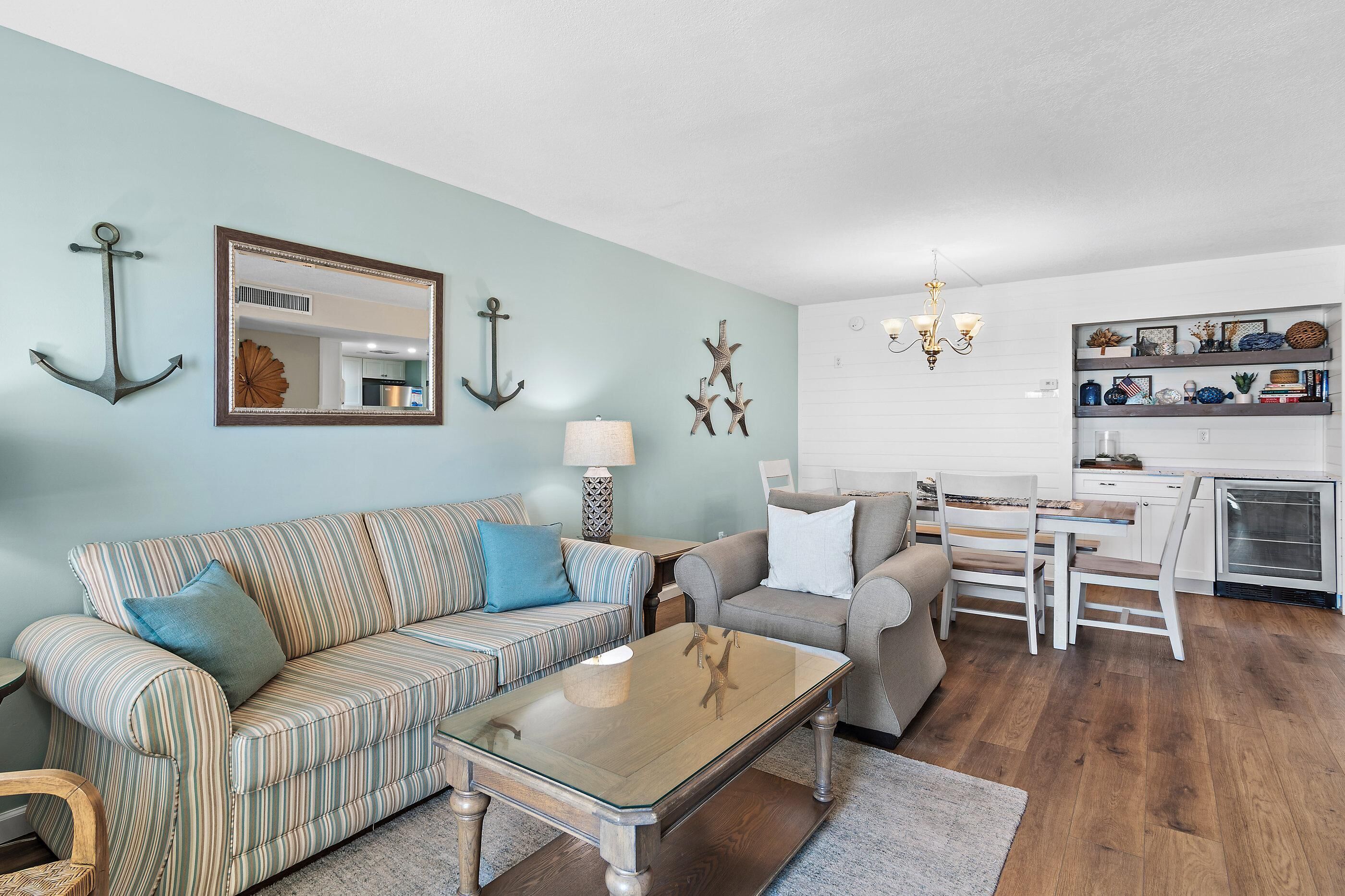 A living room with striped sofas, a glass coffee table, and a kitchen area with white cabinets and a built-in oven.