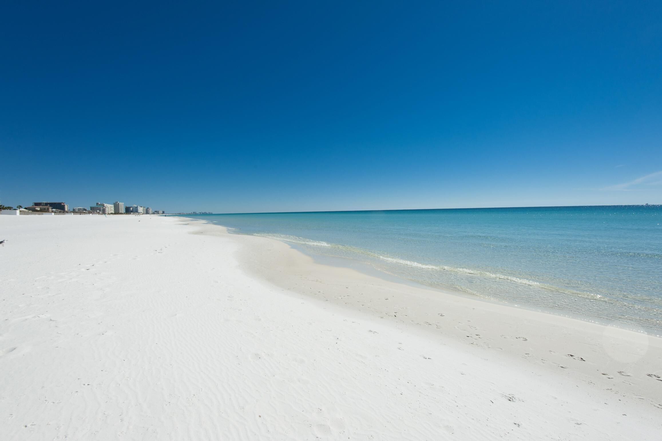 A wide, sandy beach with clear blue water and a distant city skyline.