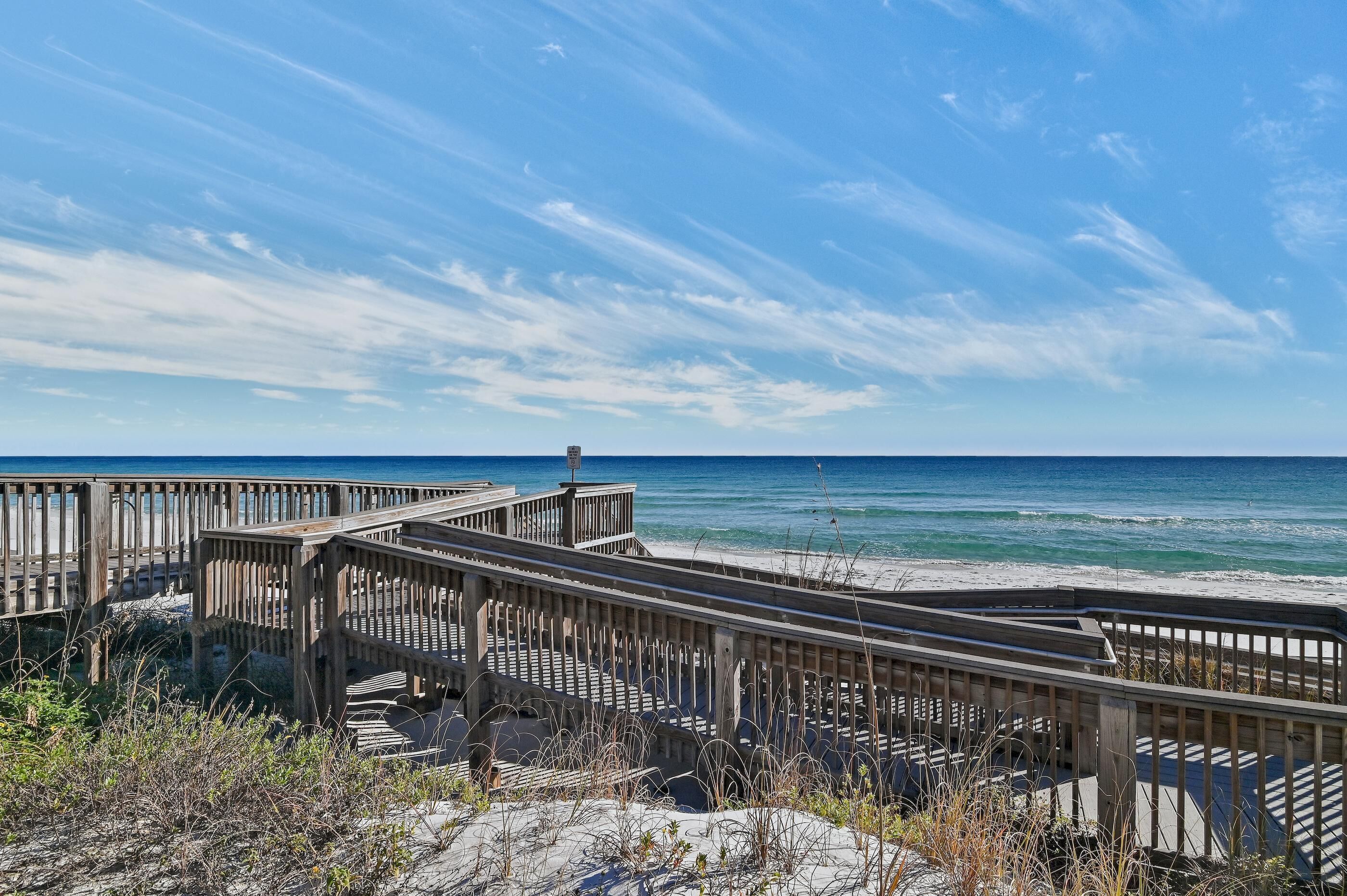 A wooden boardwalk leading to a beach with clear skies and ocean views.