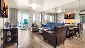 Un salón espacioso con un sofá azul, una mesa de centro de madera y un espejo grande que refleja la habitación. Hay dos lámparas sobre mesas auxiliares, y una mesa de centro de vidrio con objetos decorativos.