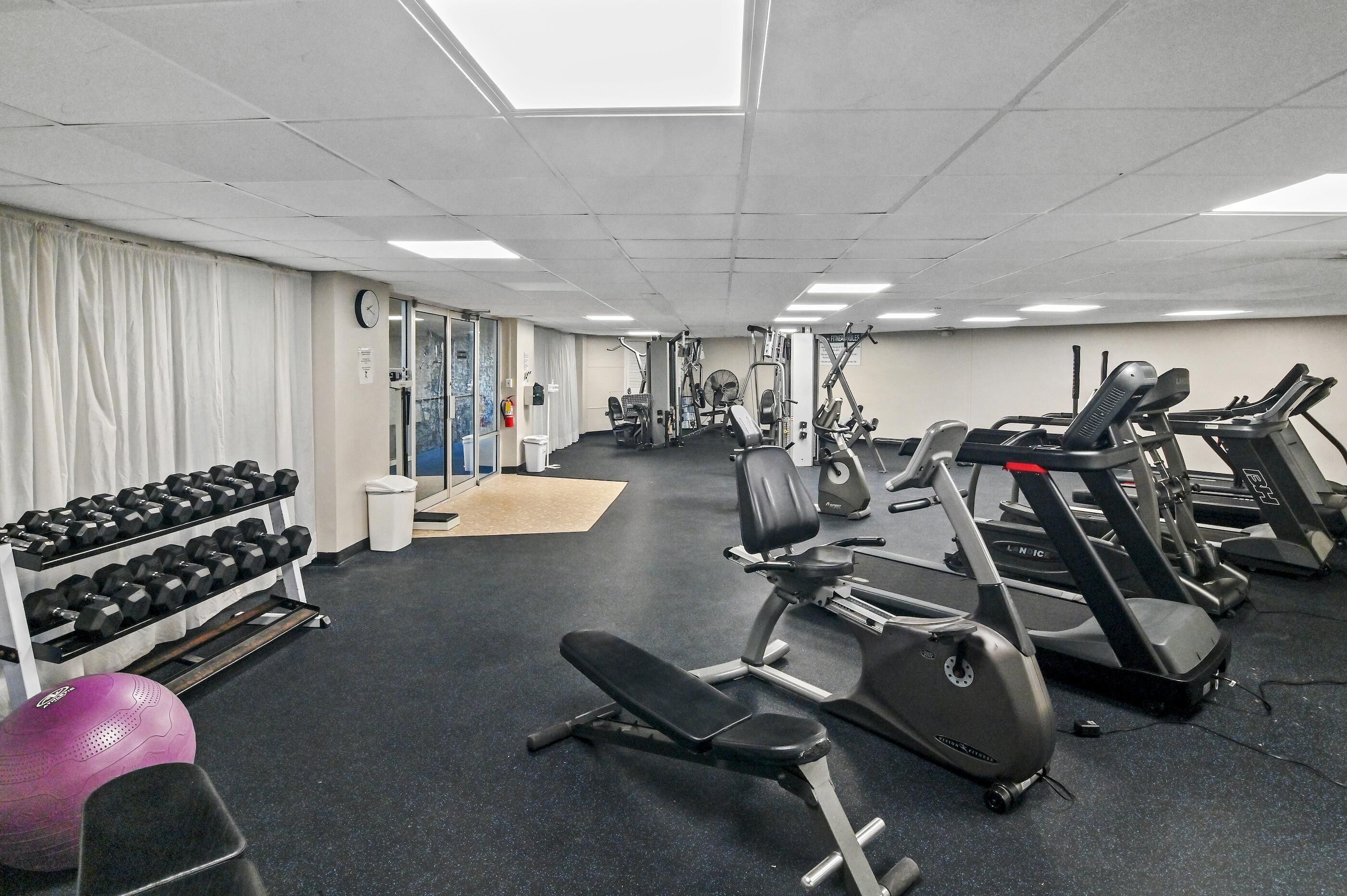 A gym with treadmills, elliptical machines, and a bench.