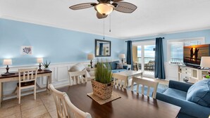 Ein Wohnzimmer mit Esstisch, Stühlen, Deckenventilator und Blick ins Freie.