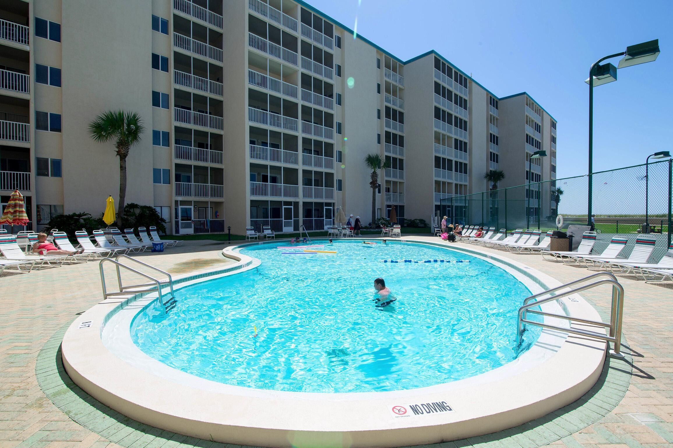 A swimming pool surrounded by lounge chairs and a multi-story building with balconies.