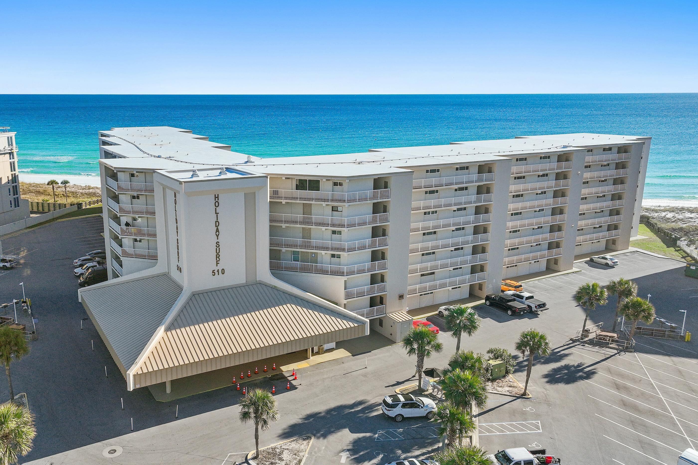 A multi-story hotel with a beach view, parking area, and a pool.