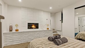 Un dormitorio moderno con chimenea, una cama con manta suave y un espejo grande.