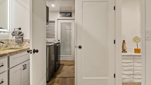 Un pasillo con una zona de cocina, una puerta con un letrero y un estante pequeño con objetos decorativos.