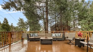 Una terraza de madera con sofá y sillones, rodeada de árboles altos.