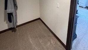 A corner room with a closet containing hanging clothes and a small shelf. - Meadowview Suite (Temecula)