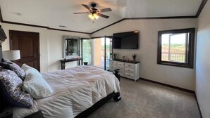 A bedroom with a bed, a ceiling fan, a TV, a window, and a desk with a chair. - Meadowview Suite (Temecula)