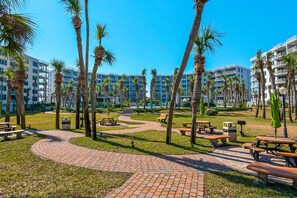 A resort with palm trees, picnic tables, and a brick pathway. - Destin West Bayside Heron 507- A Wave From It All (Fort Walton Beach)
