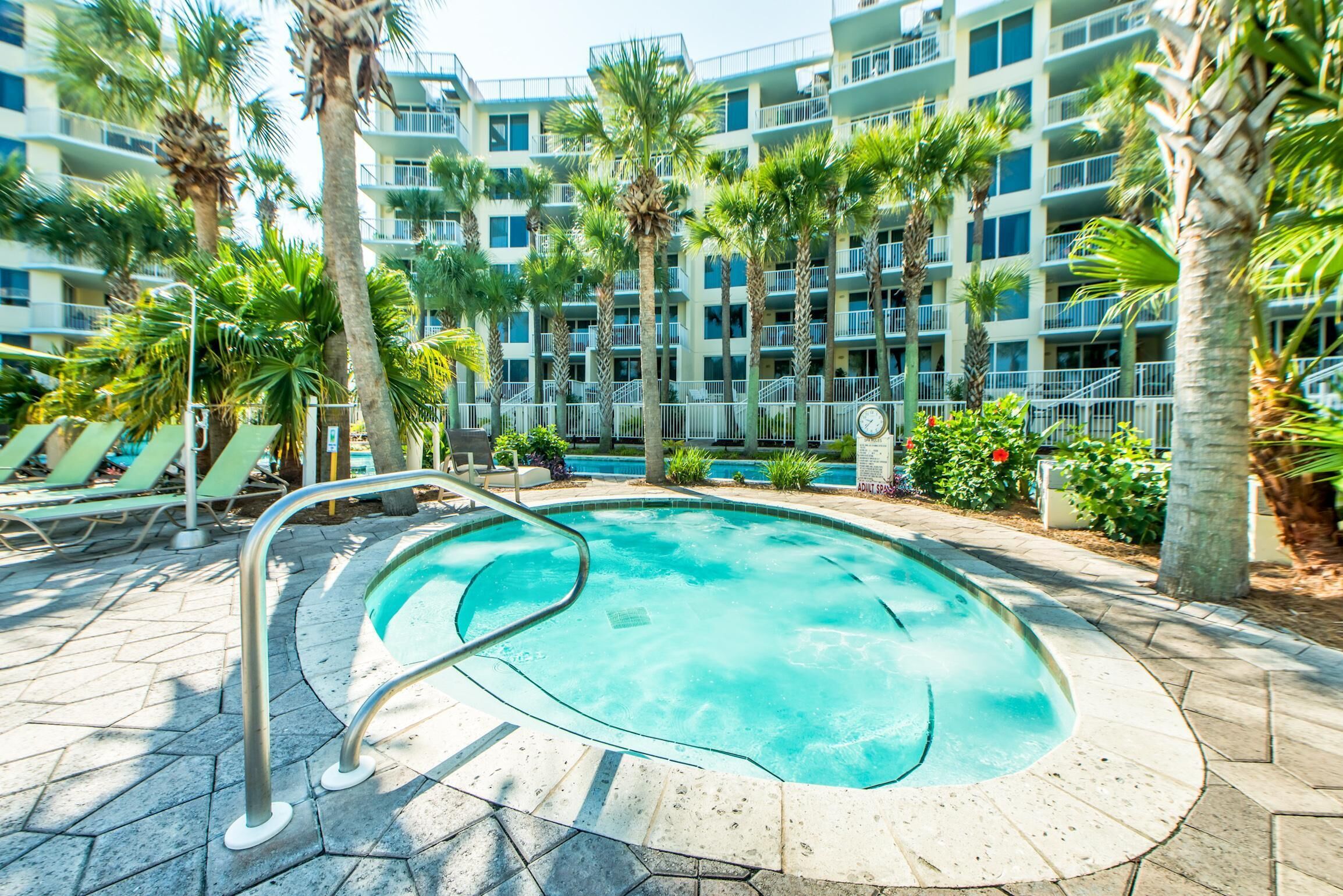 A swimming pool surrounded by palm trees and a multi-story building with balconies.