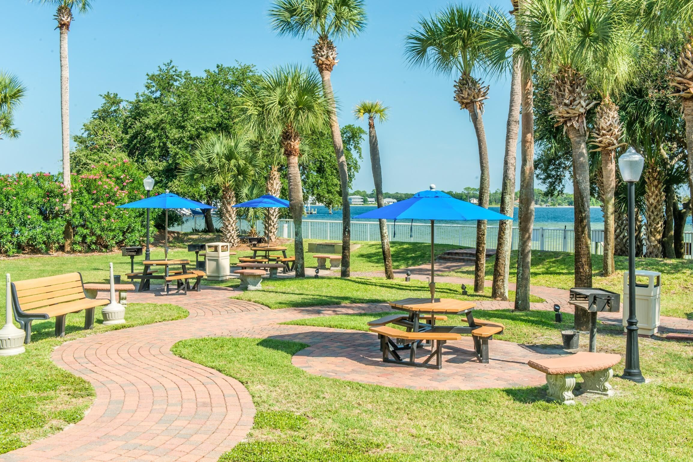 A park with picnic tables, benches, and blue umbrellas.