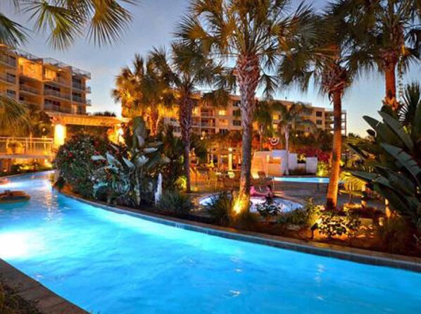 A swimming pool surrounded by palm trees and hotel buildings. - Destin West Bayside Heron 507- A Wave From It All (Fort Walton Beach)