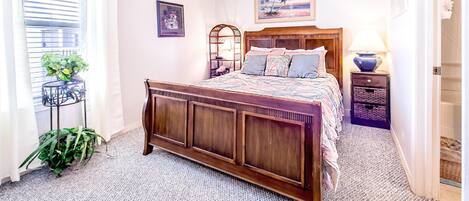 Een slaapkamer met een houten bed, een plafondventilator, een nachtkastje, een lamp en een lijst met een afbeelding aan de muur.