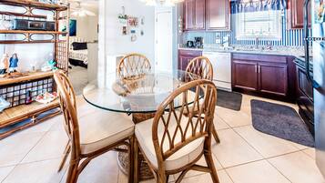 A dining area with a glass table surrounded by wicker chairs, a kitchen with dark wooden cabinets, and a window with striped curtains.
