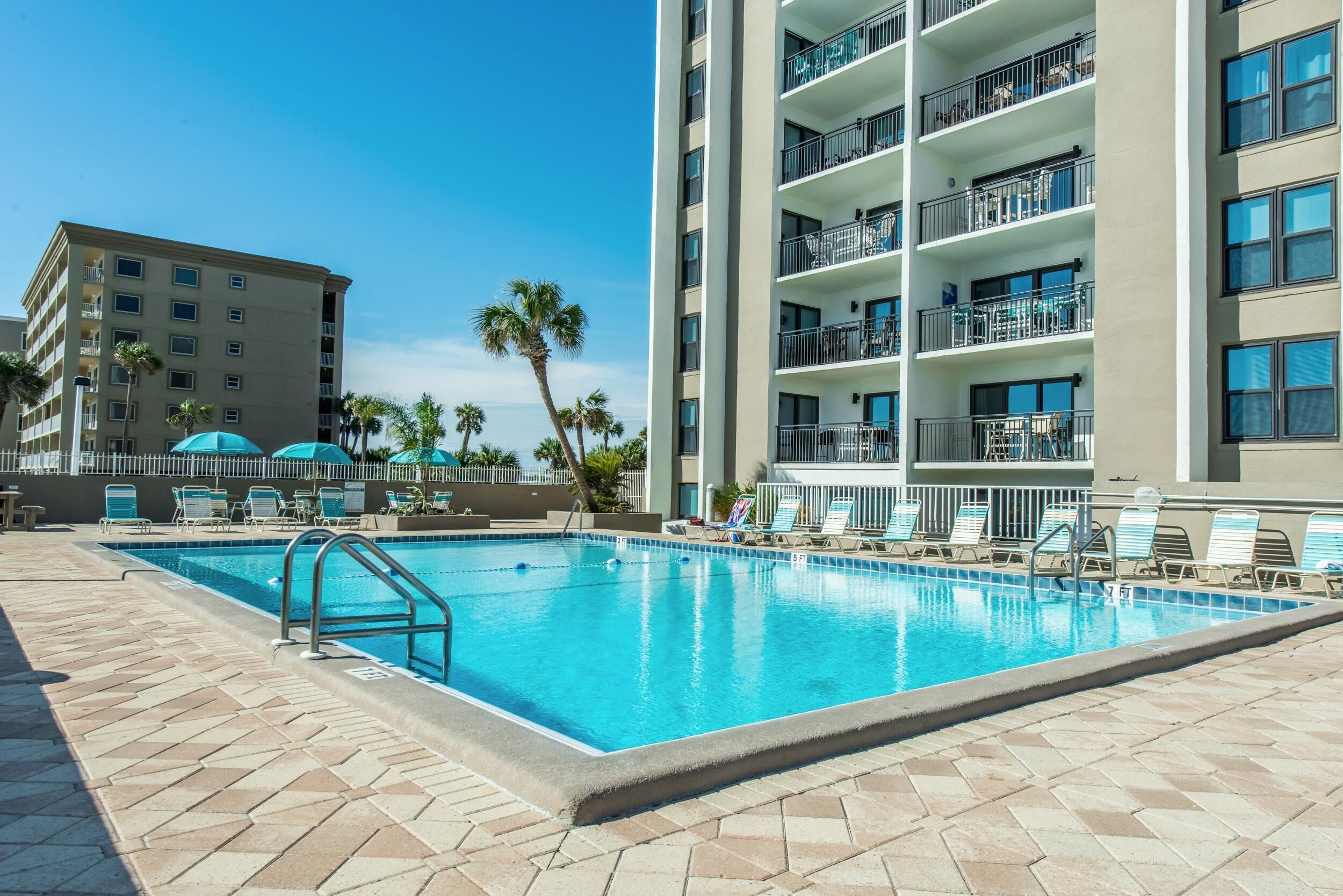 A swimming pool area with lounge chairs and a building with balconies.