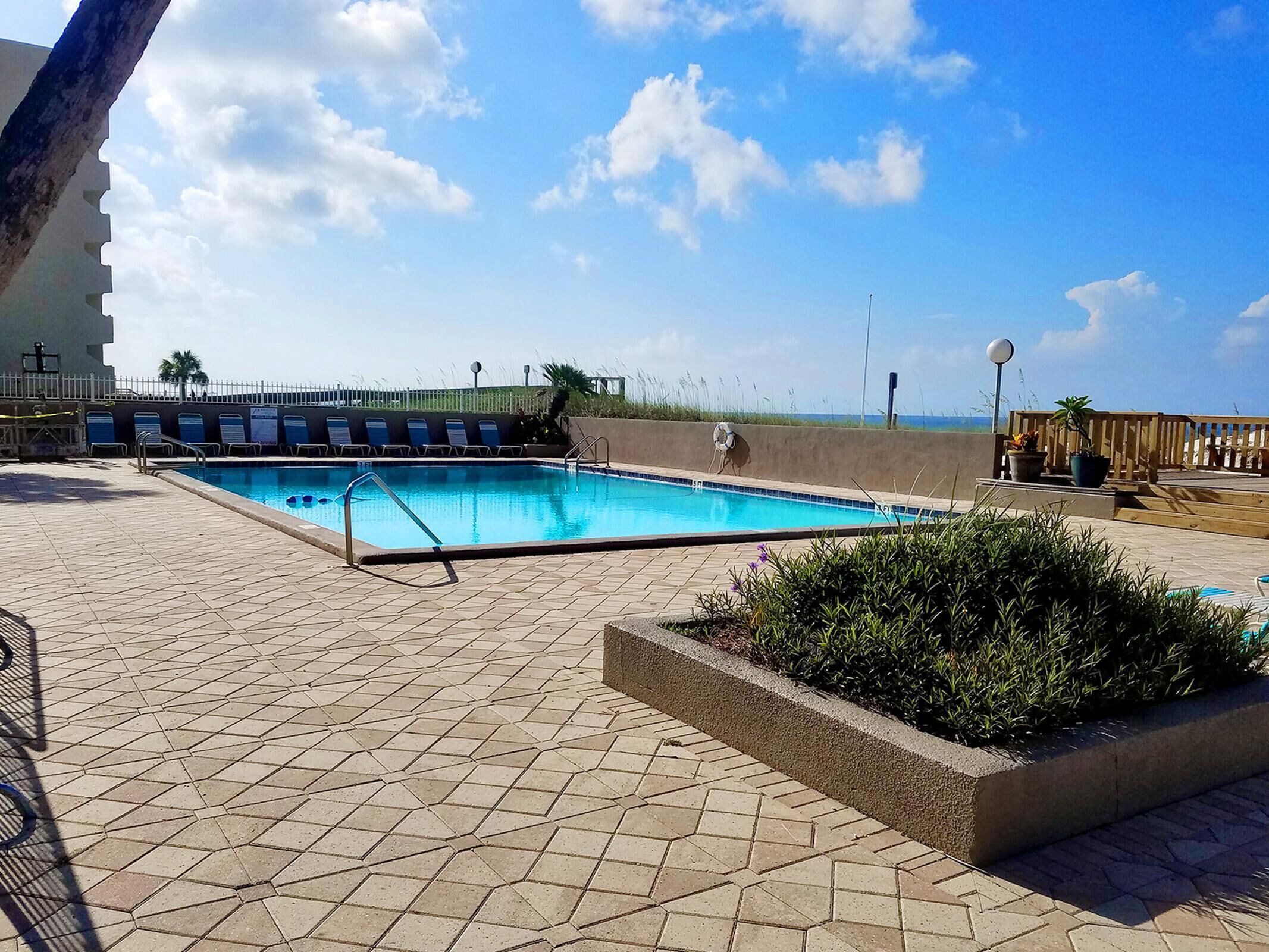 A swimming pool with a tiled deck, a wooden fence, and a view of the sea.