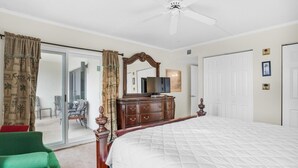 A bedroom with a large bed, a dresser, a ceiling fan, and a sliding glass door leading to a balcony. - Emerald Isle 210 (Fort Walton Beach)