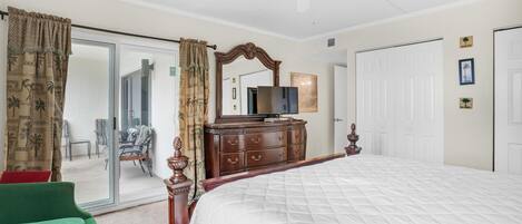 A bedroom with a large bed, a dresser, a ceiling fan, and a sliding glass door leading to a balcony.