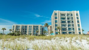 A beachfront hotel with multiple balconies, a clear view of the ocean, and a sandy beach in the foreground. - Emerald Isle 210 (Fort Walton Beach)