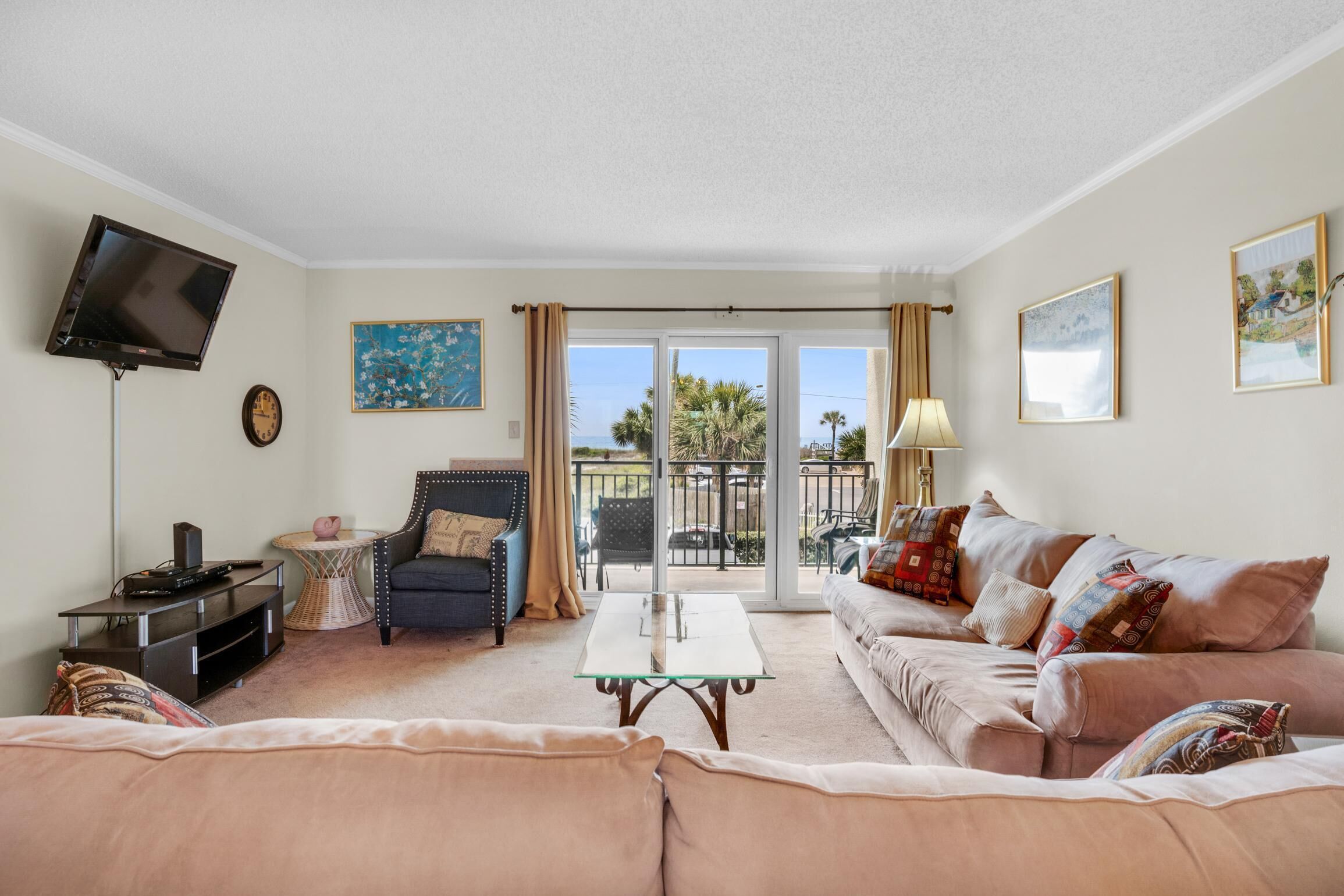 A living room with a sofa, armchair, coffee table, TV, and a balcony with outdoor furniture.