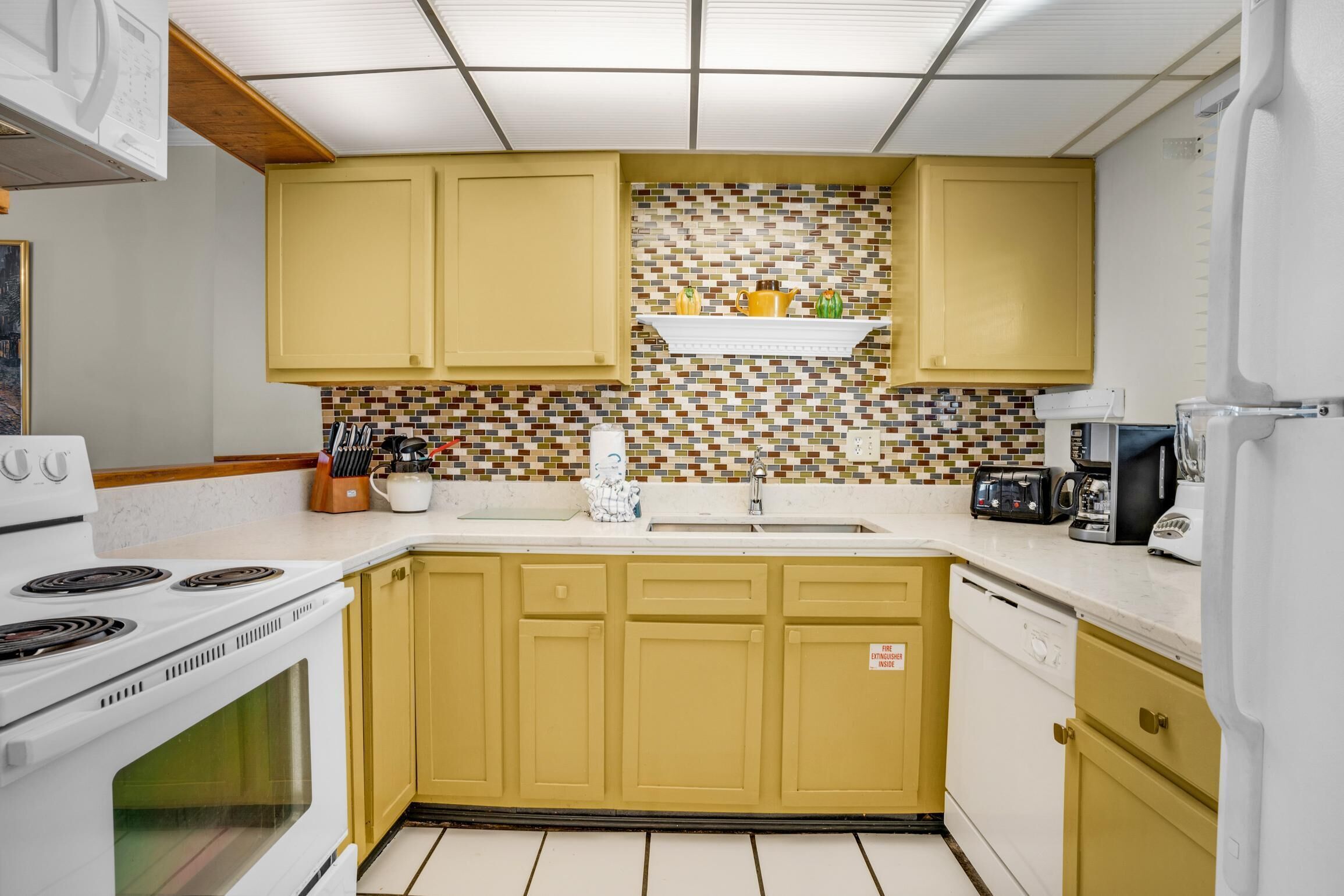 Une cuisine avec des meubles de couleur jaune, un dosseret carrelé et des appareils électroménagers blancs.
