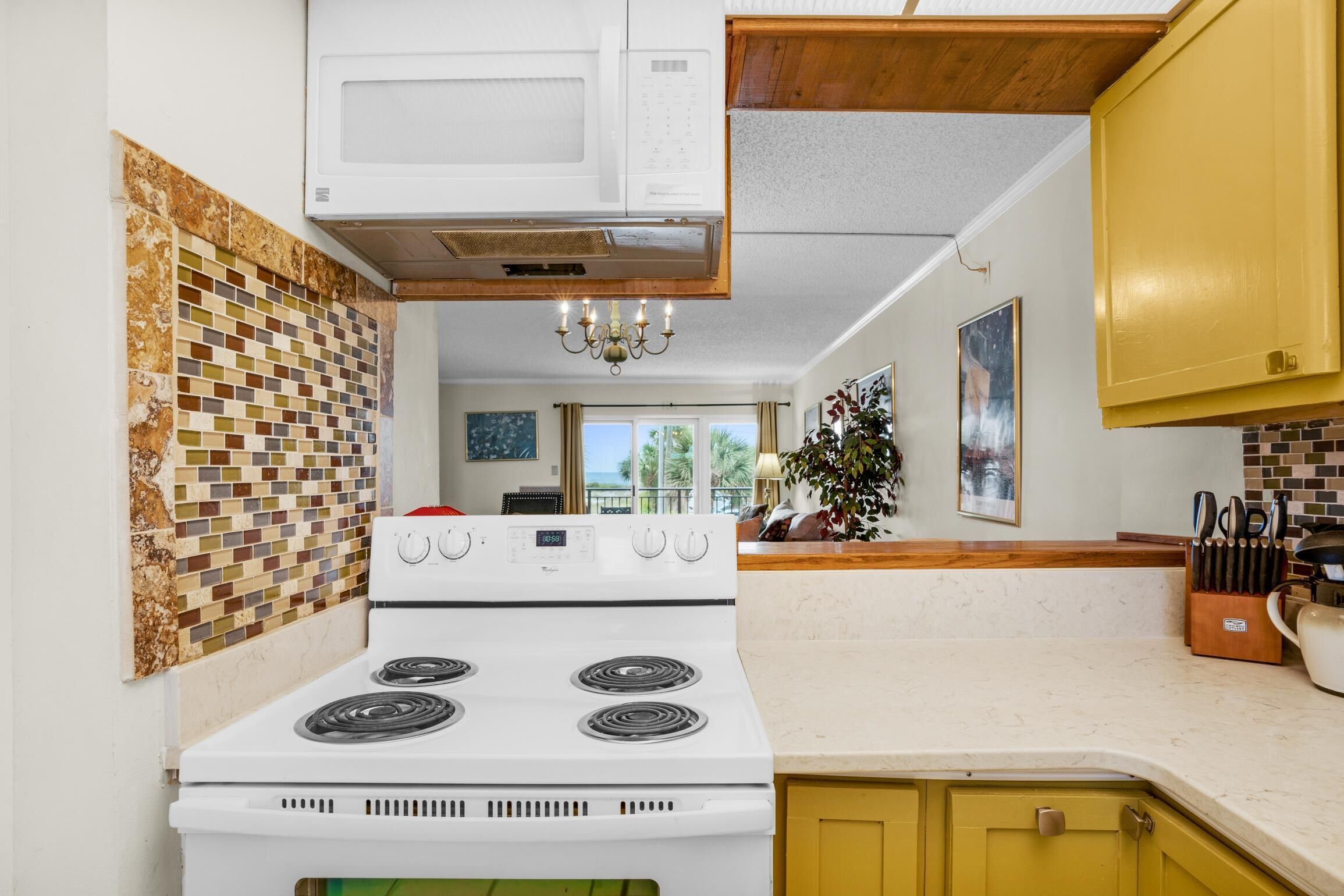 A kitchen with a white stove, yellow cabinets, and a tiled backsplash.