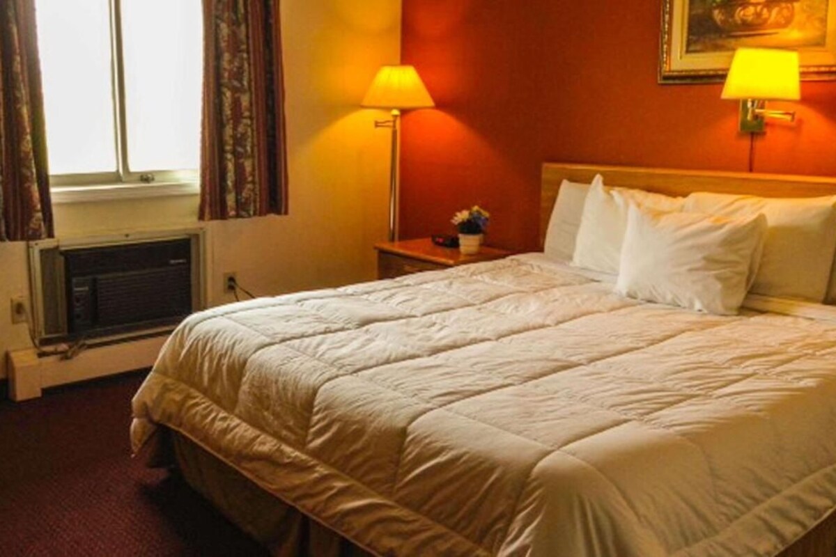 A hotel room with a large bed, two bedside lamps, a nightstand, and a window with curtains.