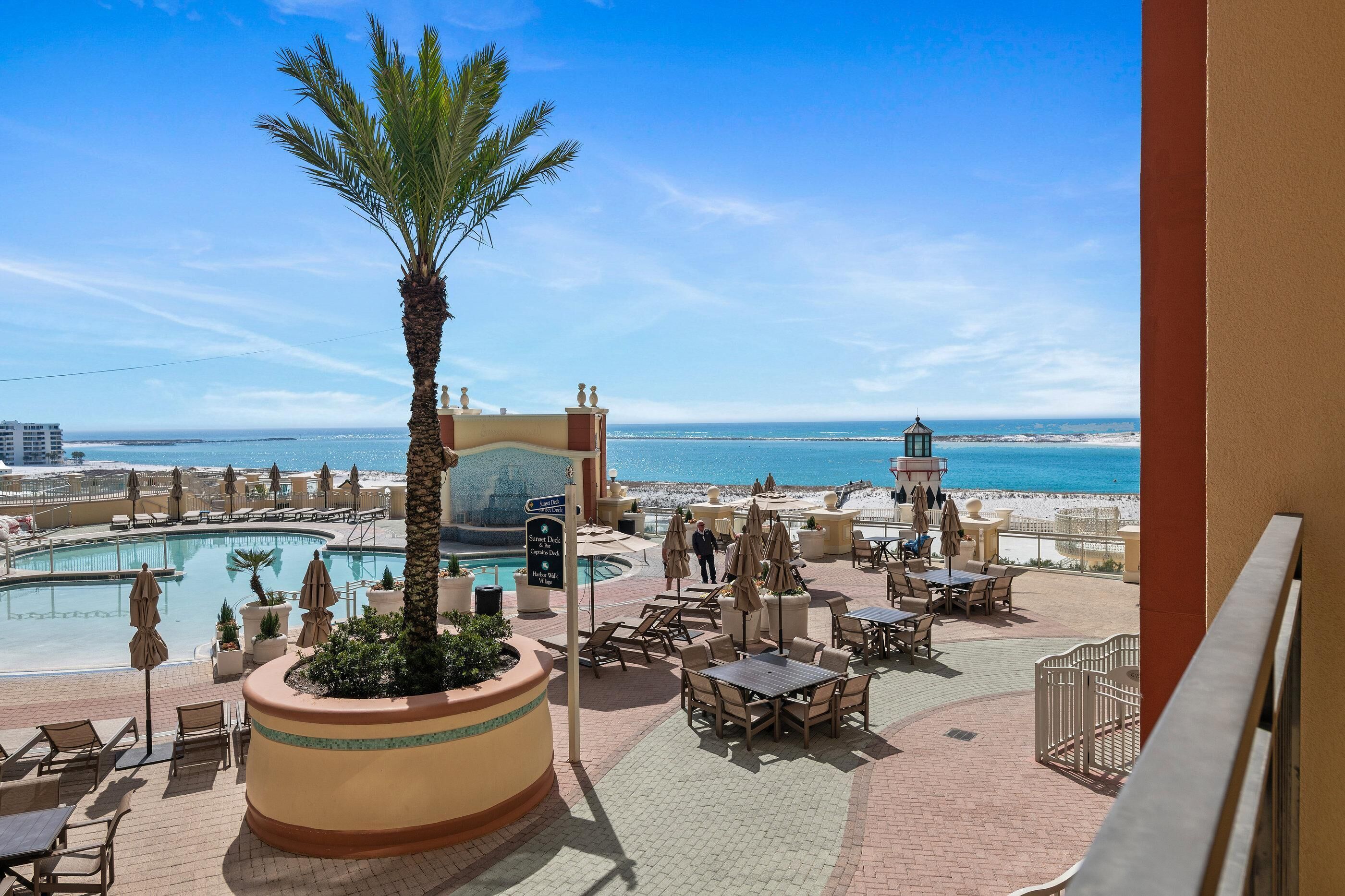 A resort pool area with lounge chairs, umbrellas, and a palm tree.