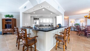 A spacious kitchen with a central island, white cabinetry, and a dining area with wooden chairs. - East Pass 605 (Destin)