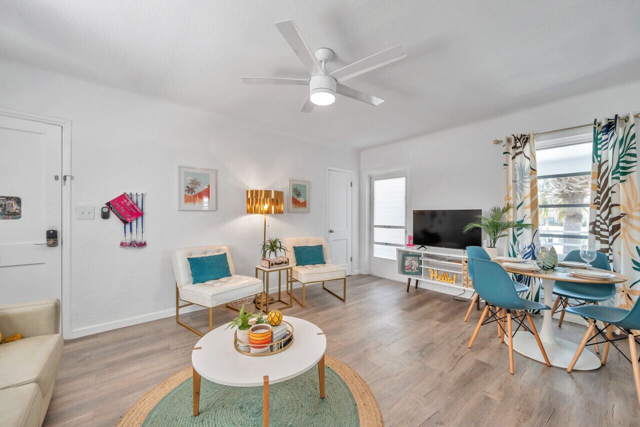 Un salon moderne doté d’un ventilateur de plafond, d’un téléviseur et d’un coin repas avec des chaises bleues et une table ronde.